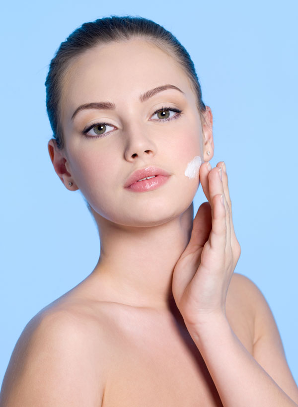 Portrait of young woman applying cream on her beautiful fresh face - blue background